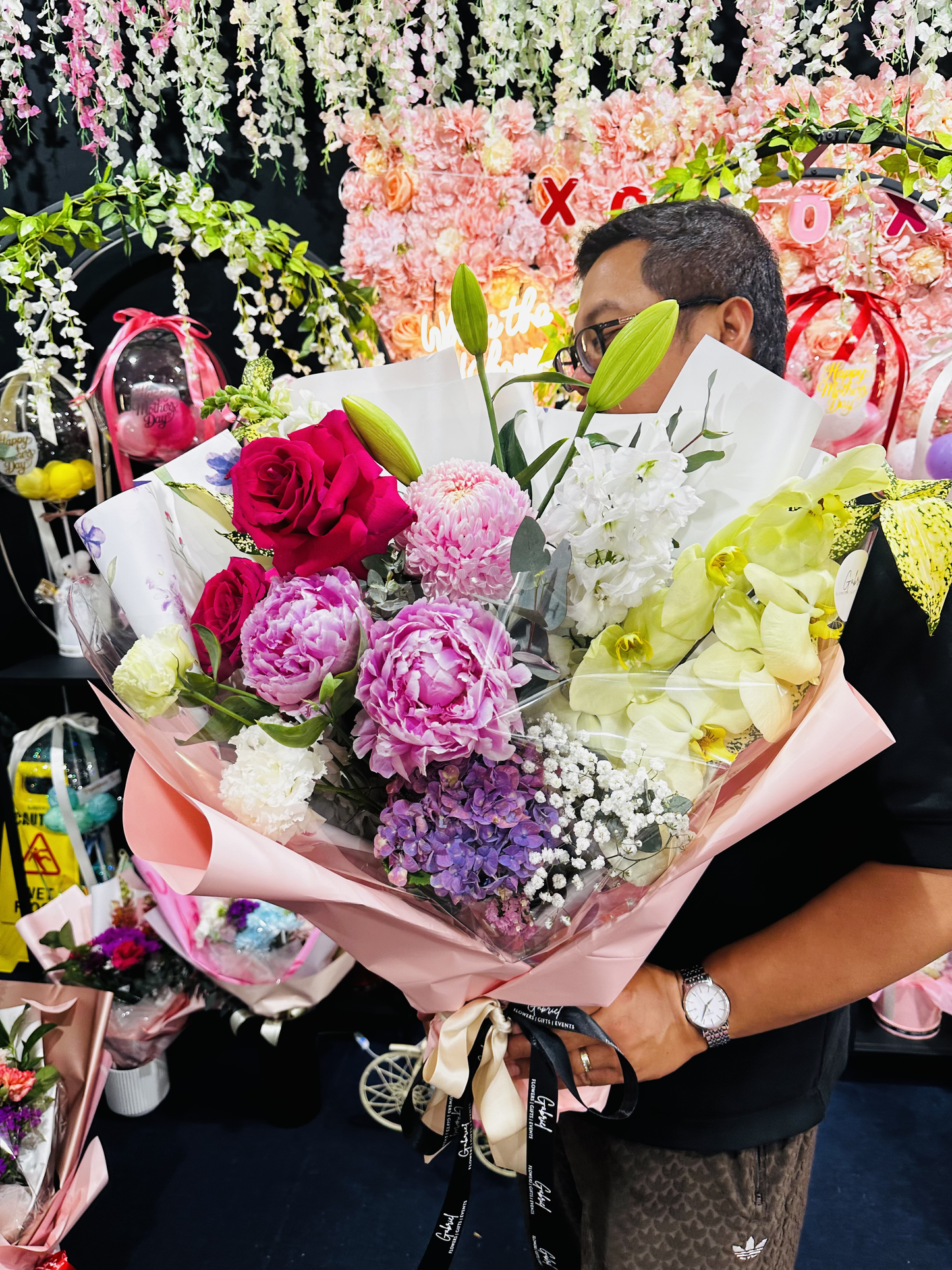 A luxurious hand-tied bouquet featuring vibrant pink roses, lush pink peonies, green cymbidium orchids, white lilies, purple hydrangea, chrysanthemums, stock flowers, and seasonal blooms, beautifully wrapped in premium pink paper with elegant ribbon. A colourful and premium floral arrangement perfect for birthdays, celebrations, anniversaries, Mother's Day, and heartfelt gifting. ๐ธ๐