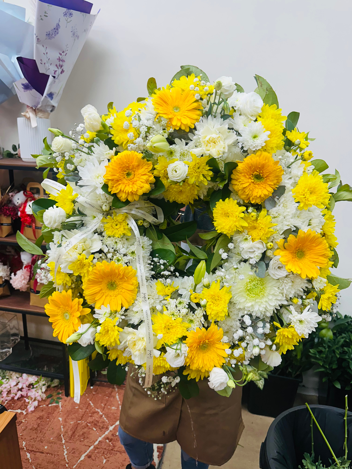 Sunshine Remembrance funeral wreath featuring bright yellow gerberas, white chrysanthemums, delicate seasonal blooms and fresh greenery, arranged in a traditional circular design.