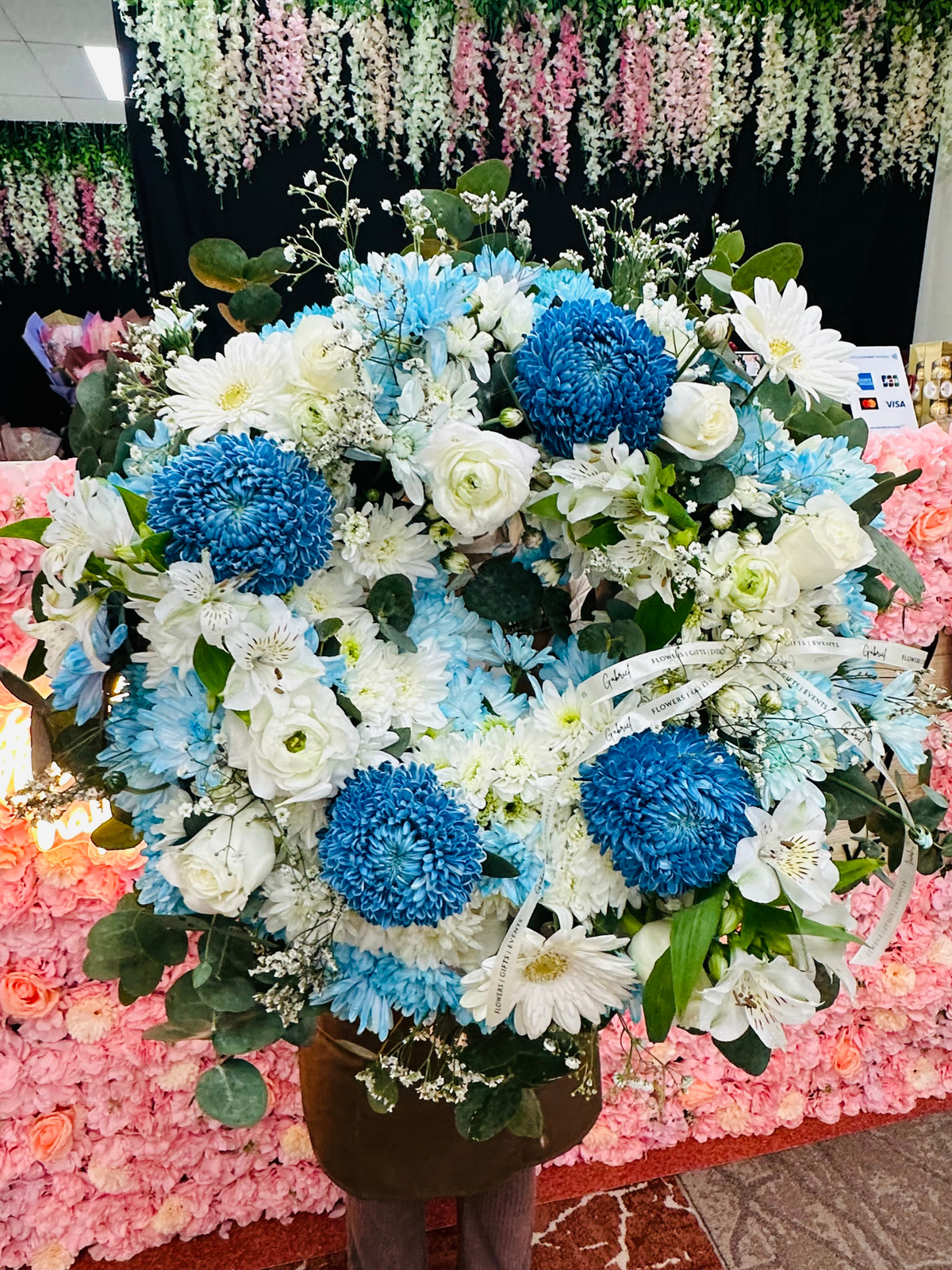 Heavenly Blue blue and white funeral wreath featuring chrysanthemums, white gerberas, roses, alstroemeria, delicate seasonal blooms and fresh eucalyptus greenery.
